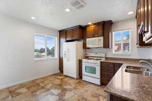 Kitchen with light tile floors, white appliances, sink, and a wealth of natural light