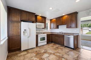 Kitchen featuring white appliances, sink, light tile flooring, and a textured ceiling