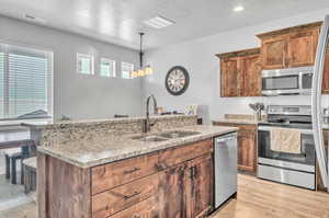 Kitchen featuring hanging light fixtures, appliances with stainless steel finishes, light hardwood / wood-style floors,  and a kitchen island with sink