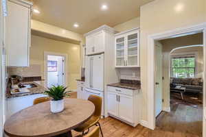 Kitchen with white fridge, light wood-type flooring, backsplash, sink, and white cabinetry