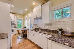 Kitchen featuring tasteful backsplash, white appliances, light wood-type flooring, sink, and white cabinets