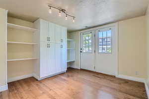 Interior space with a textured ceiling, light wood-type flooring, and rail lighting