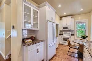 Kitchen featuring dark stone counters, light hardwood / wood-style flooring, white appliances, tasteful backsplash, and white cabinets