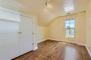 Bonus room with a textured ceiling, lofted ceiling, and hardwood / wood-style floors