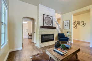 Living room featuring brick wall, wood-type flooring, a stone fireplace, and a textured ceiling