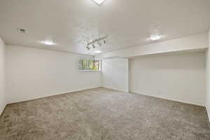 Carpeted empty room with a textured ceiling and track lighting