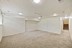 Basement featuring track lighting, light carpet, and a textured ceiling