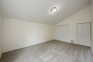 Unfurnished bedroom with two closets, carpet, and vaulted ceiling