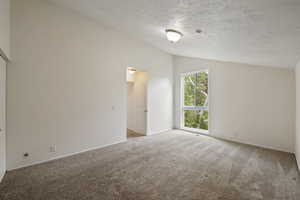 Carpeted spare room with a textured ceiling and vaulted ceiling