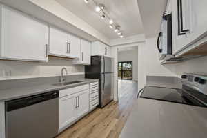 Kitchen with light hardwood / wood-style floors, stainless steel appliances, track lighting, sink, and white cabinets