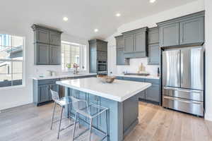 Kitchen with light hardwood / wood-style flooring, stainless steel appliances, backsplash, a center island, and a breakfast bar