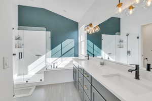 Bathroom with tile flooring, independent shower and bath, double sink vanity, an inviting chandelier, and vaulted ceiling