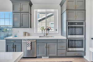 Kitchen with light hardwood / wood-style flooring, tasteful backsplash, gray cabinets, sink, and appliances with stainless steel finishes