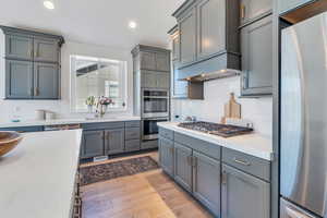 Kitchen featuring appliances with stainless steel finishes, sink, tasteful backsplash, and light wood-type flooring