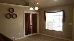 Empty room featuring a healthy amount of sunlight, carpet, vaulted ceiling, and an inviting chandelier