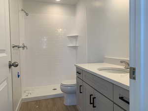 Bathroom featuring tiled shower, hardwood / wood-style flooring, vanity, and toilet