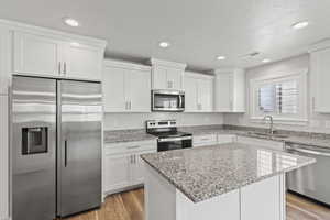 Kitchen with light wood-type flooring, stainless steel appliances, a center island, sink, and white cabinets