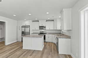 Kitchen featuring light wood-type flooring, appliances with stainless steel finishes, a kitchen island, and light stone countertops