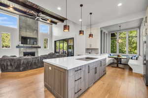 Kitchen featuring light hardwood / wood-style flooring, a center island with sink, a tiled fireplace, beamed ceiling, and pendant lighting