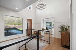 Hall featuring light wood finished floors, healthy amount of natural light, a chandelier, a wainscoted wall, and a decorative wall