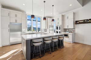 Kitchen featuring built in appliances, light countertops, backsplash, light wood-style floors, and white cabinetry