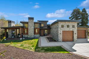 Back of house featuring stone siding, concrete driveway, a chimney, and a garage