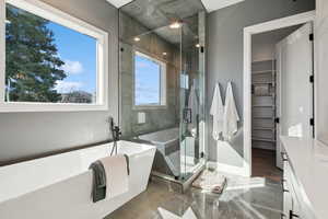 Full bathroom with a stall shower, a freestanding bath, a spacious closet, and baseboards