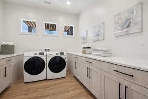 Clothes washing area with independent washer and dryer, cabinet space, light wood-style floors, and recessed lighting
