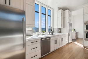 Kitchen featuring stainless steel appliances, a sink, backsplash, light wood finished floors, and light countertops