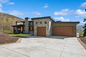 Contemporary house featuring concrete driveway, a mountain view, a garage, and stone siding