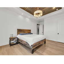 Bedroom with a tray ceiling, wooden ceiling, wood-type flooring, and a chandelier