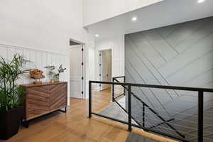Corridor featuring a decorative wall, an upstairs landing, wood finished floors, a towering ceiling, and a wainscoted wall