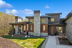 Back of property with a chimney, stone siding, and a lawn