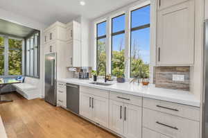 Kitchen featuring light wood-type flooring, stainless steel appliances, a healthy amount of sunlight, sink, and tasteful backsplash