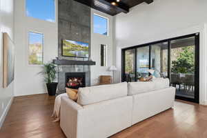 Living area featuring a towering ceiling, plenty of natural light, a tile fireplace, wood-type flooring, and beamed ceiling