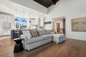 Living room with hardwood / wood-style floors, recessed lighting, beam ceiling, high vaulted ceiling, and baseboards