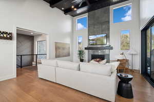 Living area with a high ceiling, plenty of natural light, wood finished floors, a fireplace, and beamed ceiling