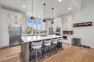 Kitchen featuring decorative light fixtures, a kitchen island, light wood-type flooring, appliances with stainless steel finishes, and a breakfast bar