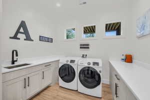 Laundry room with cabinets, light hardwood / wood-style flooring, hookup for a washing machine, independent washer and dryer, and sink