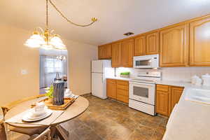 Kitchen with sink, an inviting chandelier, tasteful backsplash, pendant lighting, and white appliances