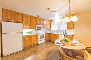 Kitchen featuring white appliances, backsplash, sink, decorative light fixtures, and a notable chandelier