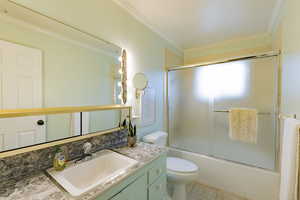 Full bathroom with vanity, tile patterned floors, crown molding, toilet, and enclosed tub / shower combo