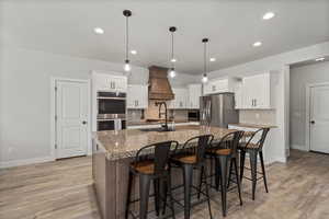 Kitchen light wood-style floors, tasteful backsplash, a spacious island, gas range, pot filler and appliances with stainless steel finishes