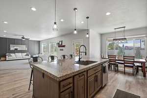 Kitchen with light wood-style flooring, dishwasher, hanging light fixtures, a center island with sink, and dining area