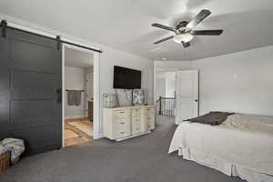 Primary bedroom featuring a barn door, ceiling fan, ensuite bath, and carpet