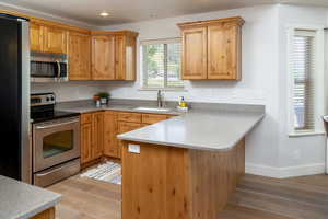 Kitchen with appliances with stainless steel finishes, light hardwood floors, sink, and kitchen peninsula