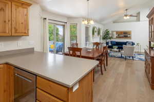 Kitchen with light hardwood floors, ceiling fan with notable chandelier, dishwasher, lofted ceiling, and pendant lighting