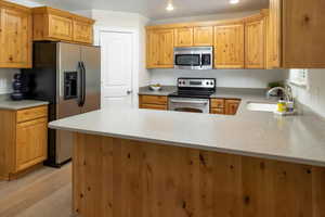 Kitchen featuring stainless steel appliances, kitchen peninsula, light wood flooring, and sink