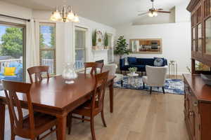 Dining area featuring ceiling fan with notable chandelier, light hardwood floors, and lofted ceiling