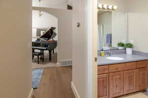 Bathroom with vaulted ceiling, vanity, and hardwood flooring & view of front entry